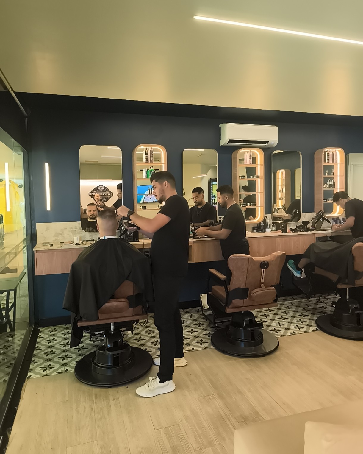 Barbeiros atendendo clientes lado a lado no salão do Sudoeste